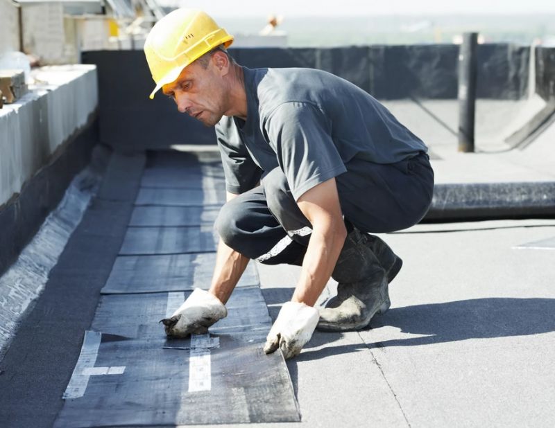 Монтажник ремонтирует крышу многоэтажного дома